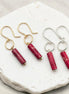 Two pairs of earrings with red cylindrical stones on a white stone surface