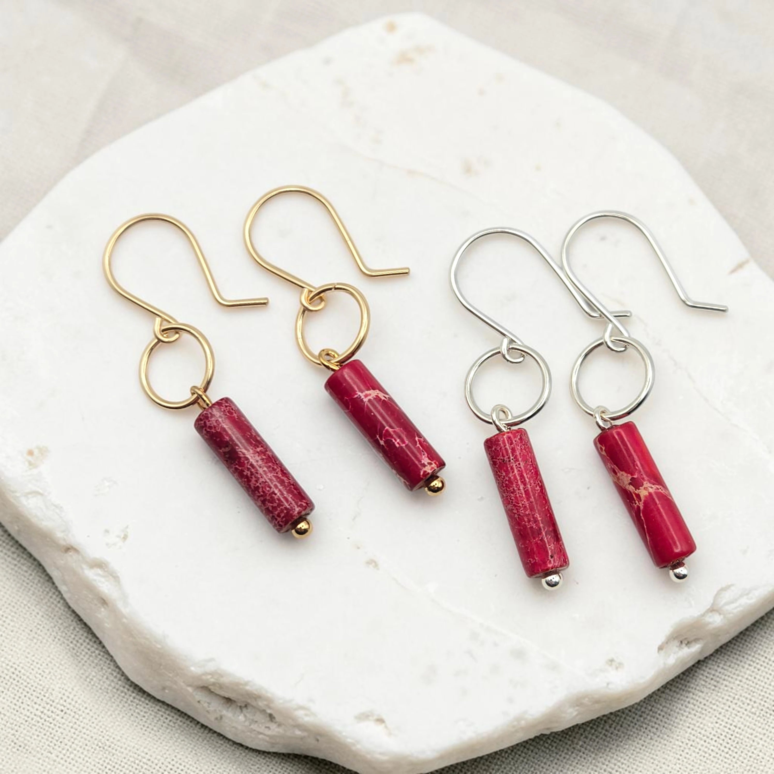 Two pairs of earrings with red cylindrical stones on a white stone surface