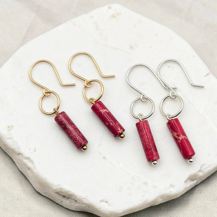 Two pairs of earrings with red cylindrical stones on a white stone surface