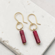 Gold earrings with red cylindrical beads on a white marble surface