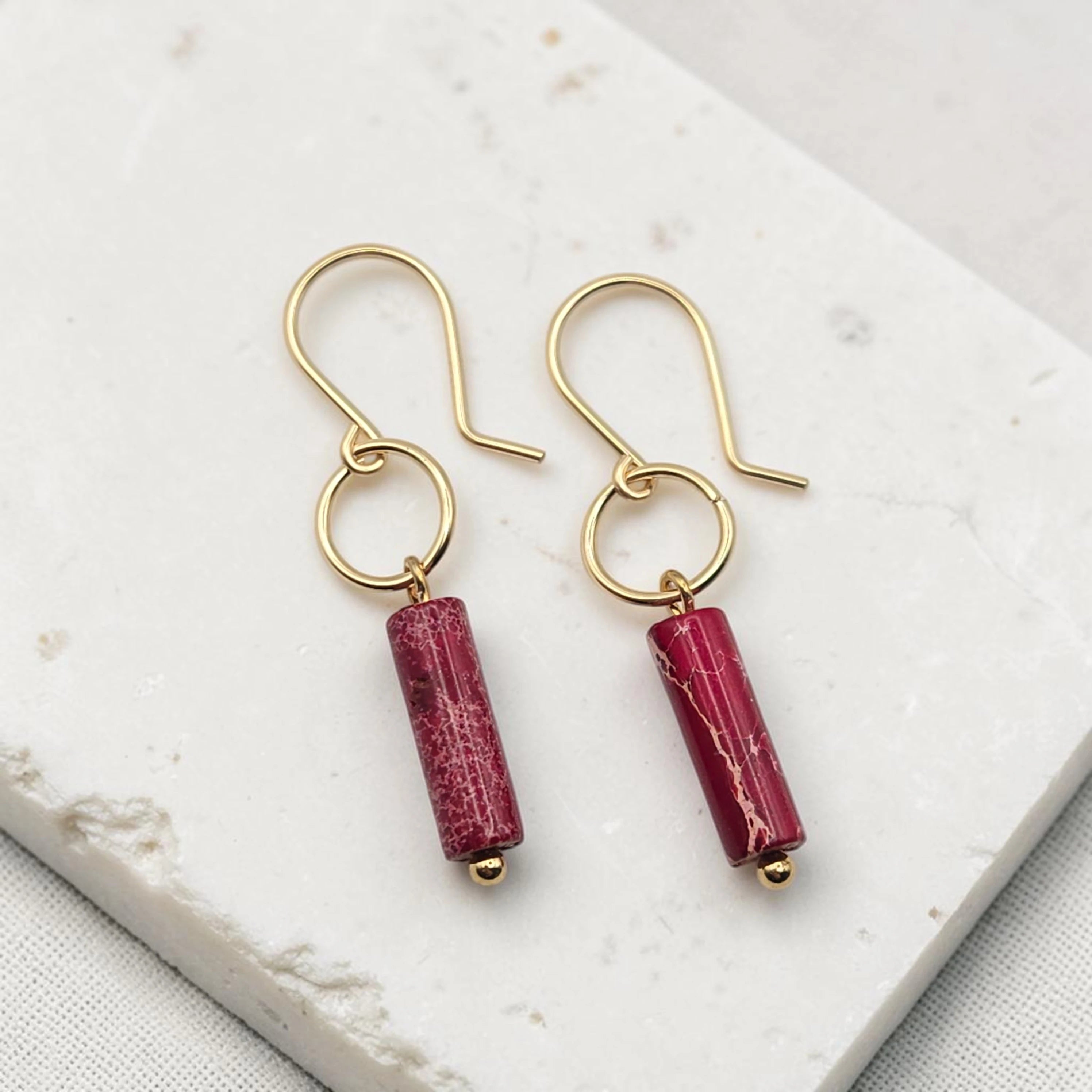 Gold earrings with red cylindrical beads on a white marble surface