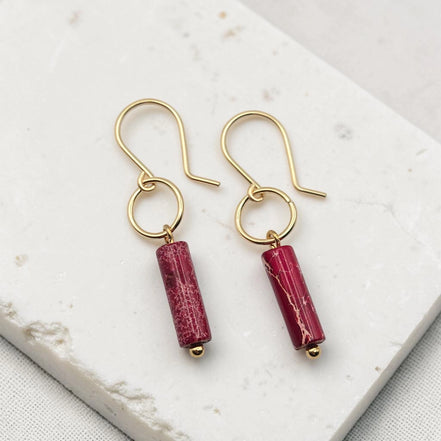 Gold earrings with red cylindrical beads on a white marble surface