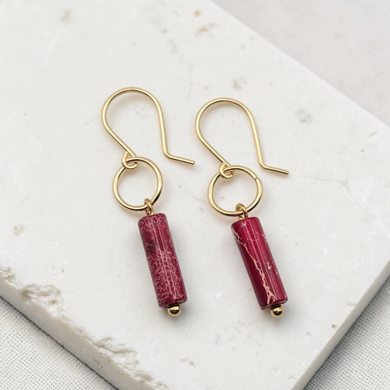 Gold earrings with red cylindrical beads on a white marble surface