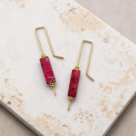 Pair of earrings with red cylindrical beads and gold hooks on a marble surface