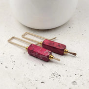 Pair of earrings with red stone and gold accents on a light surface