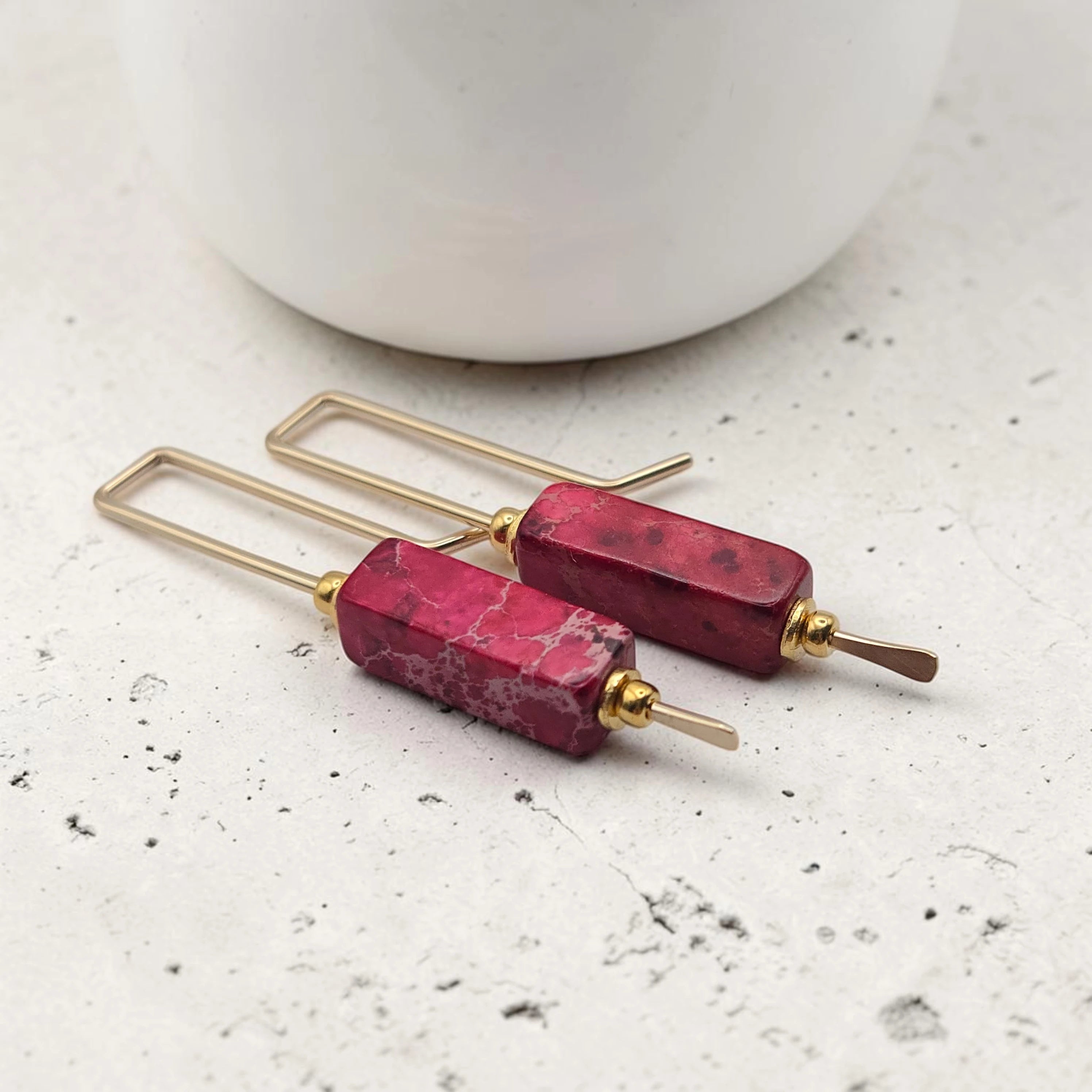 Pair of earrings with red stone and gold accents on a light surface