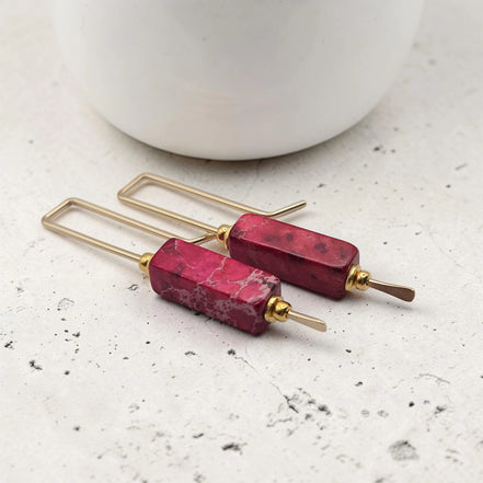 Pair of earrings with red stone and gold accents on a light surface