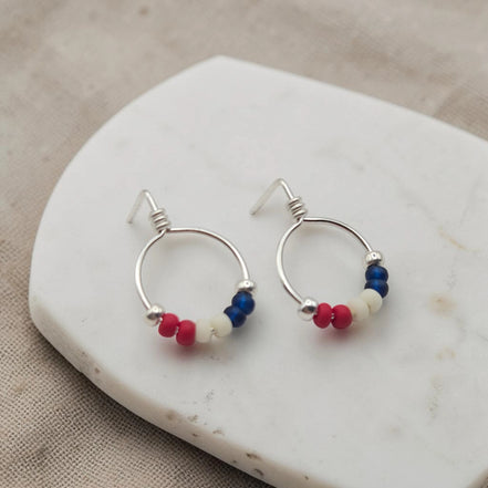 Silver hoop earrings with red white and blue beads on a marble surface