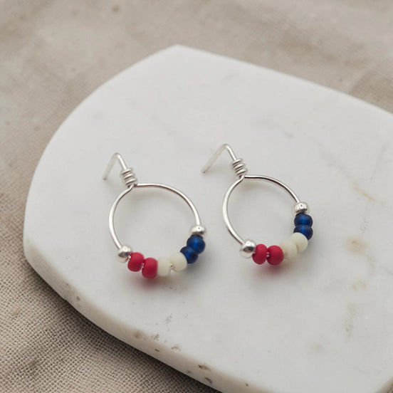 Silver hoop earrings with red white and blue beads on a marble surface