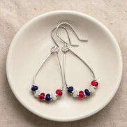 Pair of silver earrings with red, white, and blue beads on a beige surface.