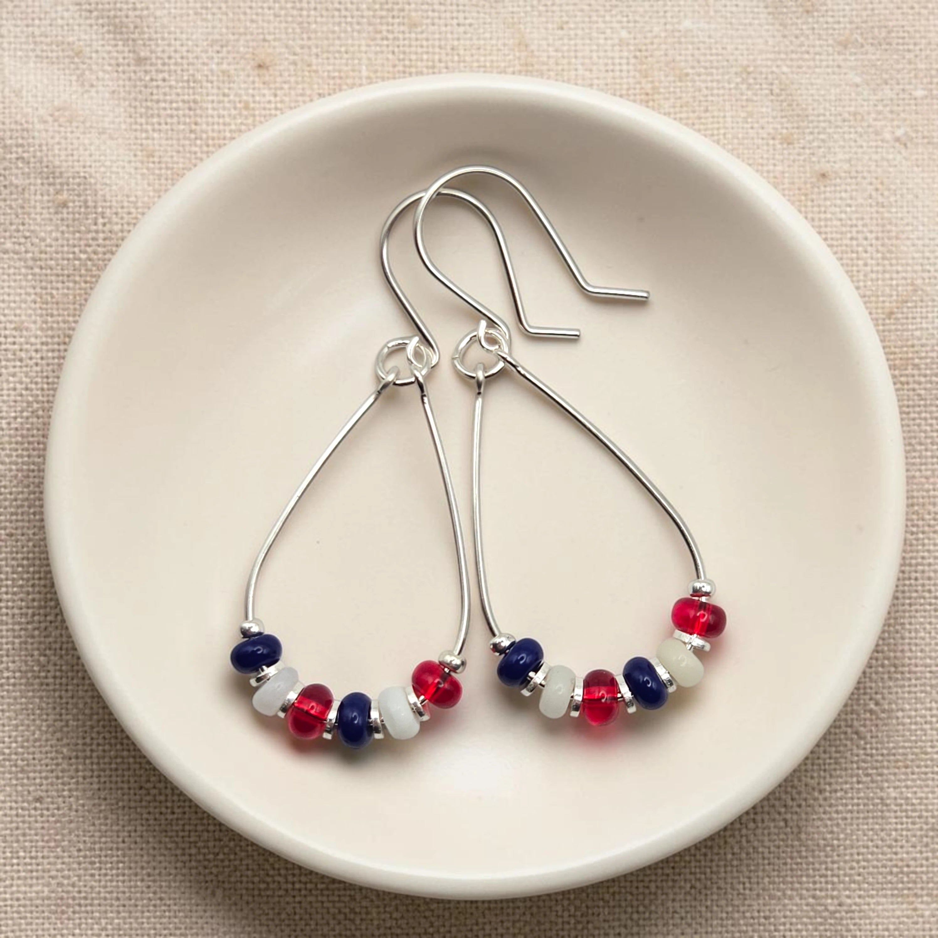 Pair of silver earrings with red, white, and blue beads on a beige surface.