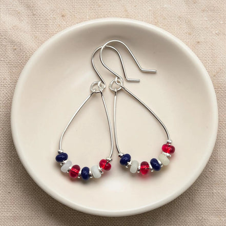 Pair of silver earrings with red, white, and blue beads on a beige surface.