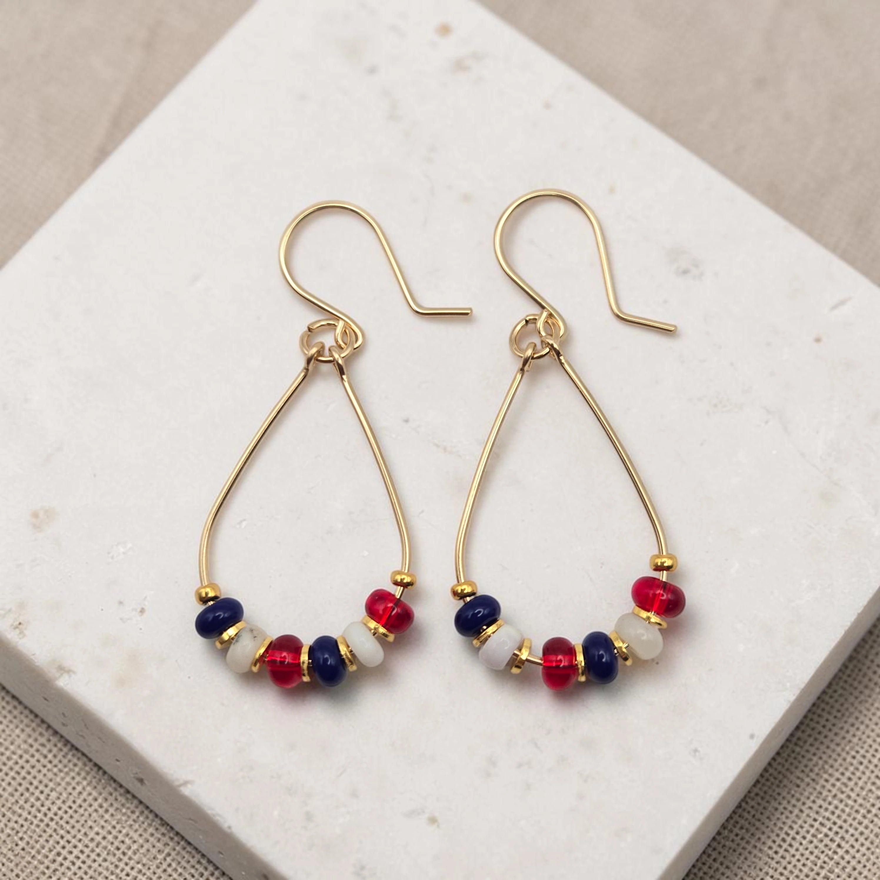 Gold hoop earrings with red, white, and blue beads on a marble surface