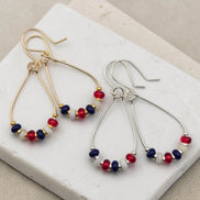 Pair of earrings with red, white, and blue beads on a white stone surface.