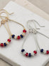 Pair of earrings with red, white, and blue beads on a white stone surface.