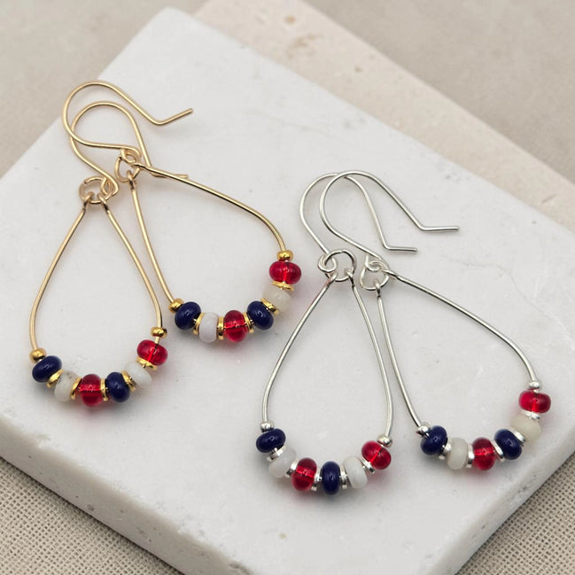 Pair of earrings with red, white, and blue beads on a white stone surface.