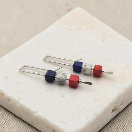 Set of earrings with red white and blue cube beads on a stone surface
