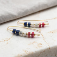 Pair of gold earrings with colorful  red white and blue beads on a marble surface