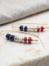 Pair of gold earrings with colorful  red white and blue beads on a marble surface