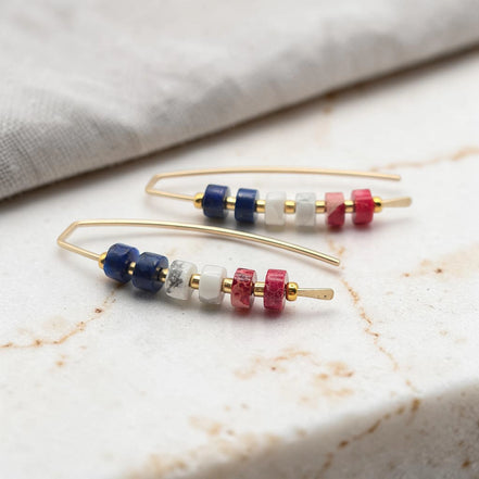 Pair of gold earrings with colorful  red white and blue beads on a marble surface