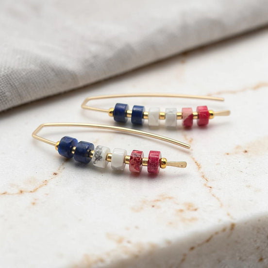 Pair of gold earrings with colorful  red white and blue beads on a marble surface