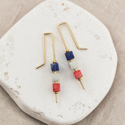 Pair of earrings with gold hooks, blue, and red beads on a white stone surface.