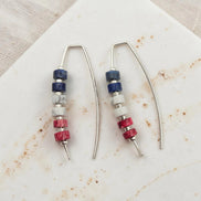 Pair of earrings with red white and blue bead accents on a textured surface