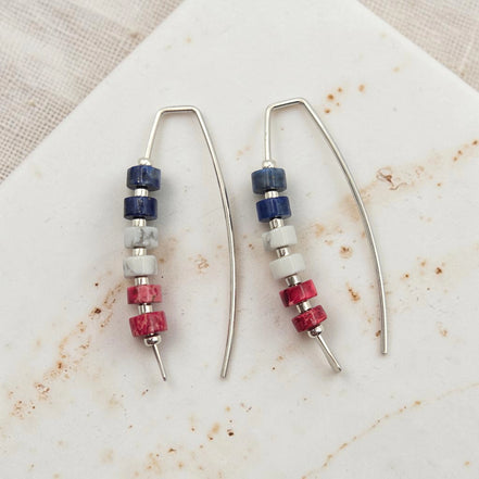 Pair of earrings with red white and blue bead accents on a textured surface