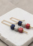 Pair of earrings with colorful cube beads on a white stone surface