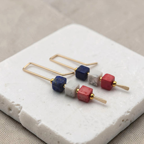Pair of earrings with colorful cube beads on a white stone surface