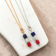 Two necklaces with red white and blue beads on a marble surface
