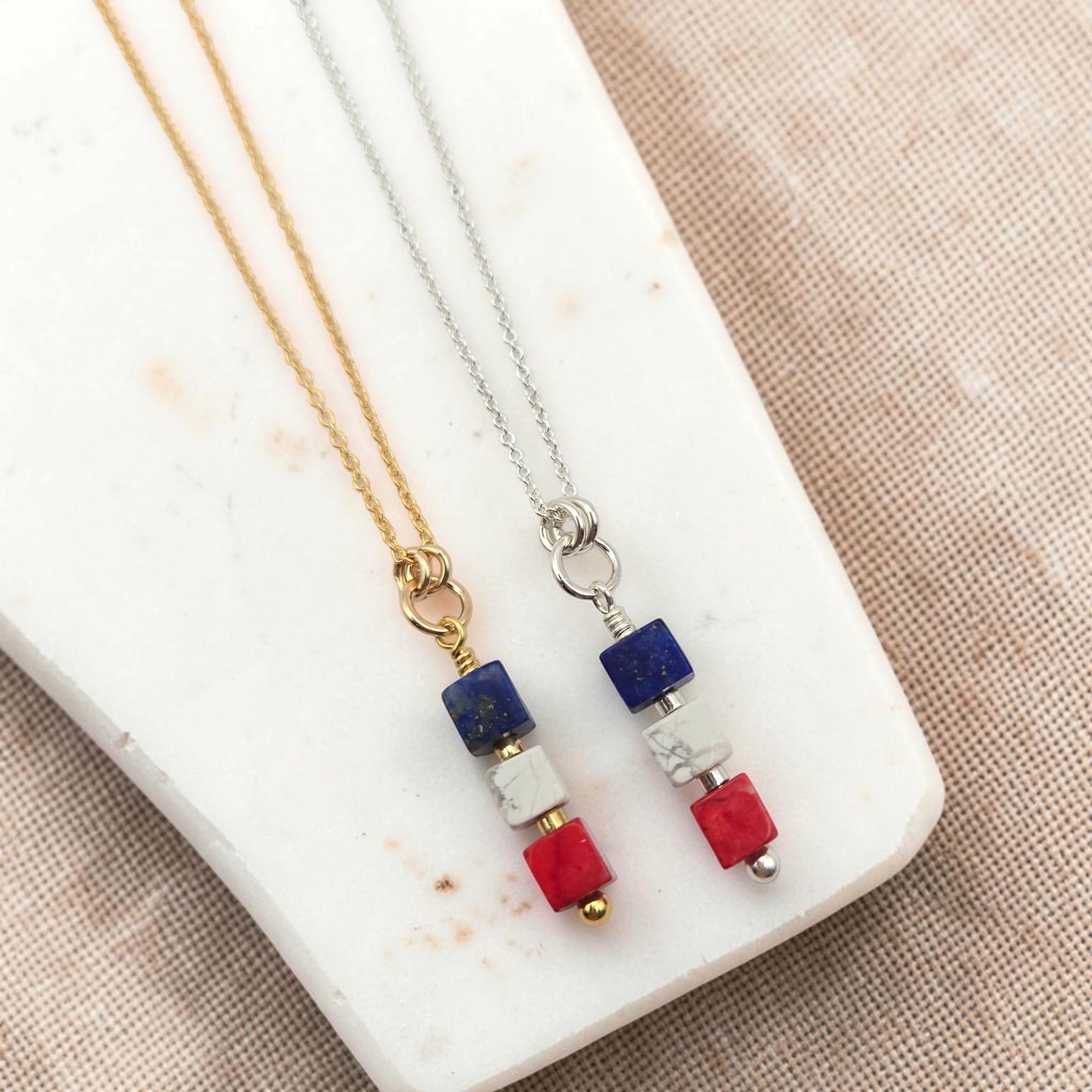 Two necklaces with red white and blue beads on a marble surface