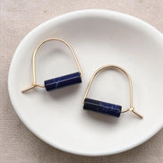 Pair of gold earrings with blue cylindrical stones on a white dish.