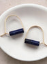 Pair of gold earrings with blue cylindrical stones on a white dish.