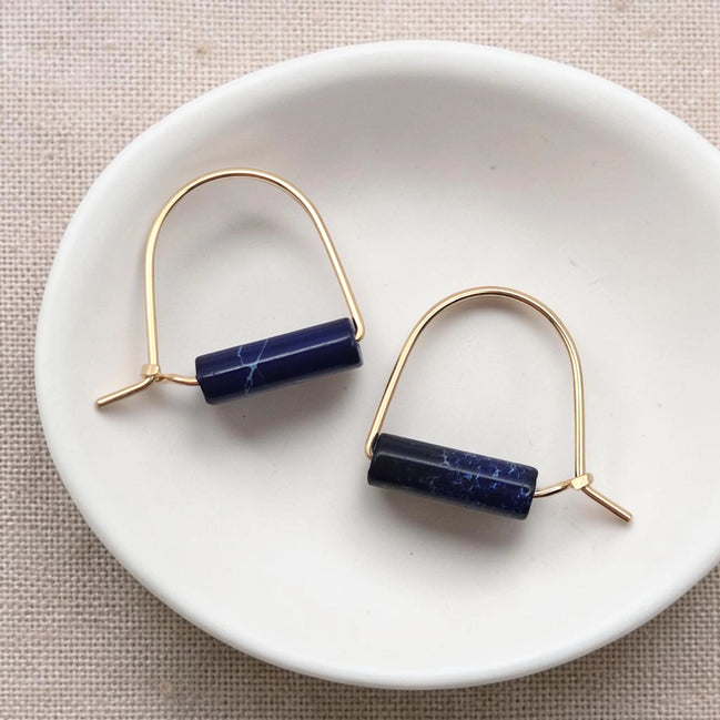 Pair of gold earrings with blue cylindrical stones on a white dish.