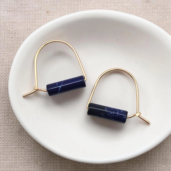 Pair of gold earrings with blue cylindrical stones on a white dish.