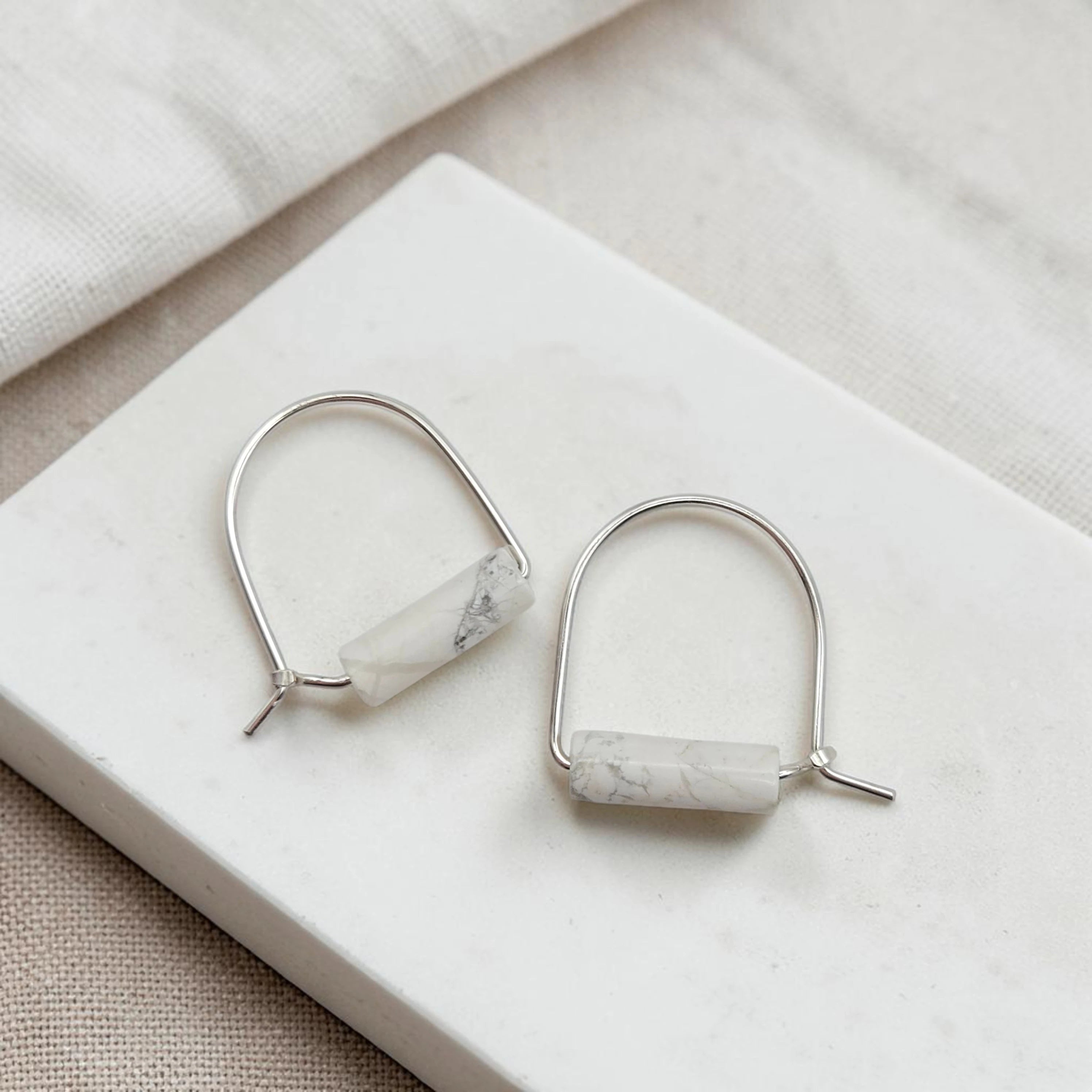 Pair of silver earrings with marble-like stones on a white surface.