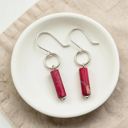 Red cylindrical earrings on a white plate with a beige background