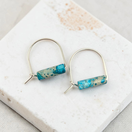 Pair of earrings with turquoise cylindrical beads on a marble surface