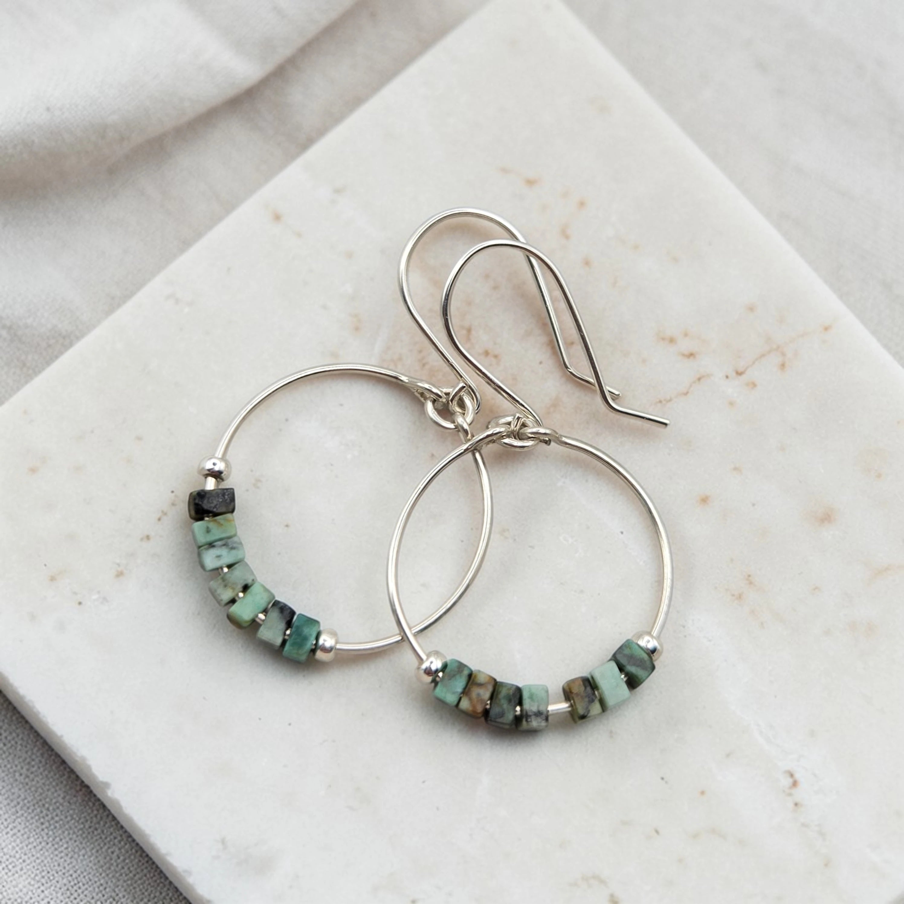 Silver hoop earrings with turquoise beads on a marble surface