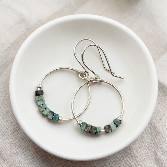 Silver hoop earrings with turquoise beads on a white dish.