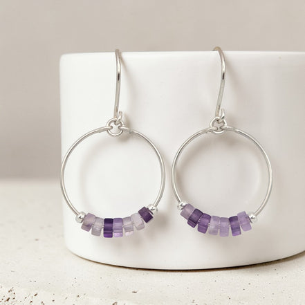 Silver hoop earrings with amethyst purple beads on a white surface