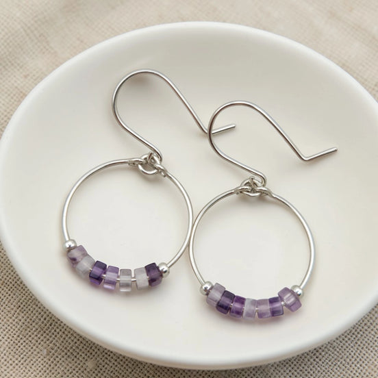 Silver hoop earrings with amethyst beads on a white plate.