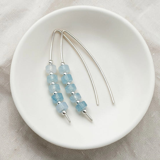 Beaded aquamarine earrings on a white plate with a beige background