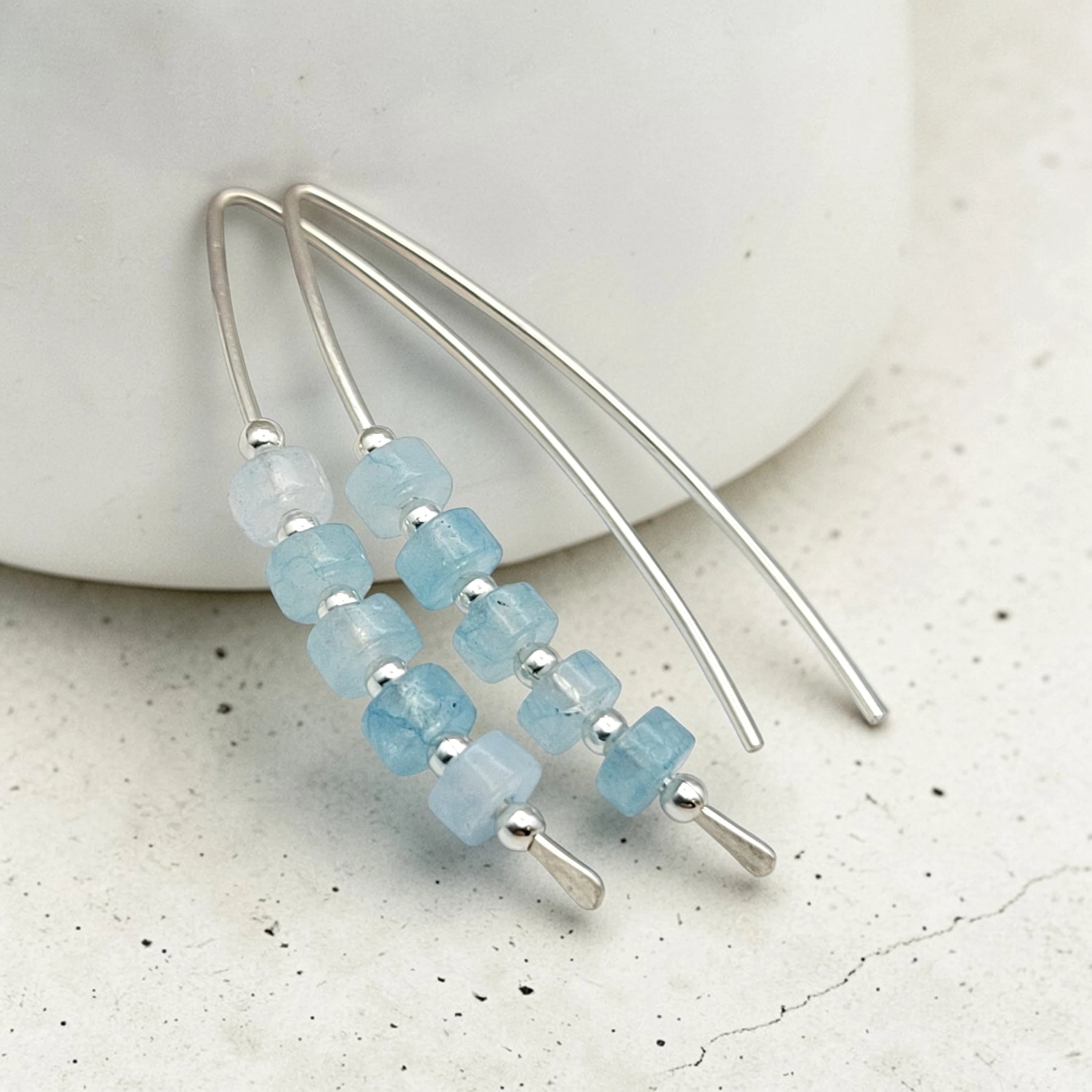 Silver earrings with blue beads on a light background