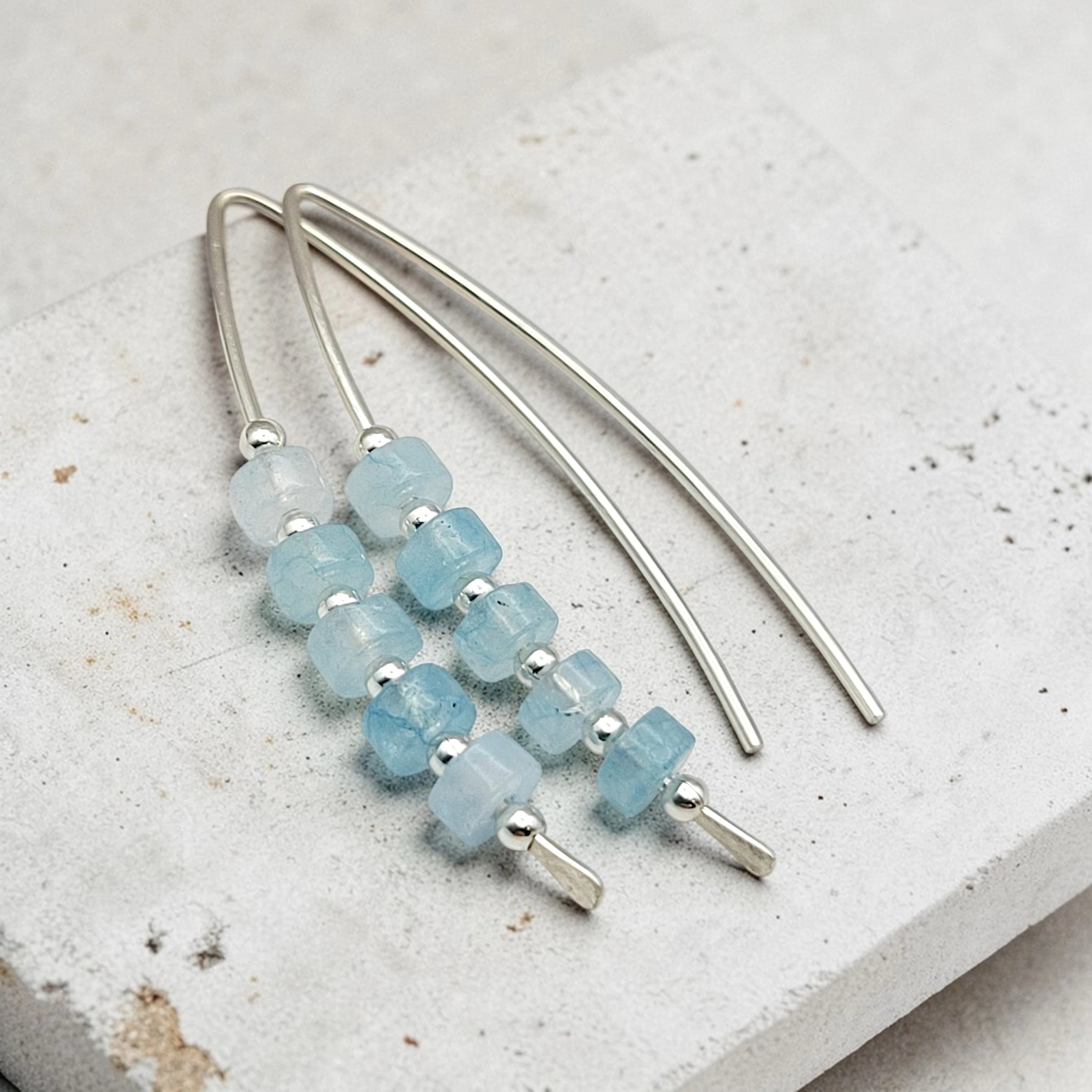 Earrings with blue beads and silver hooks on a light stone surface