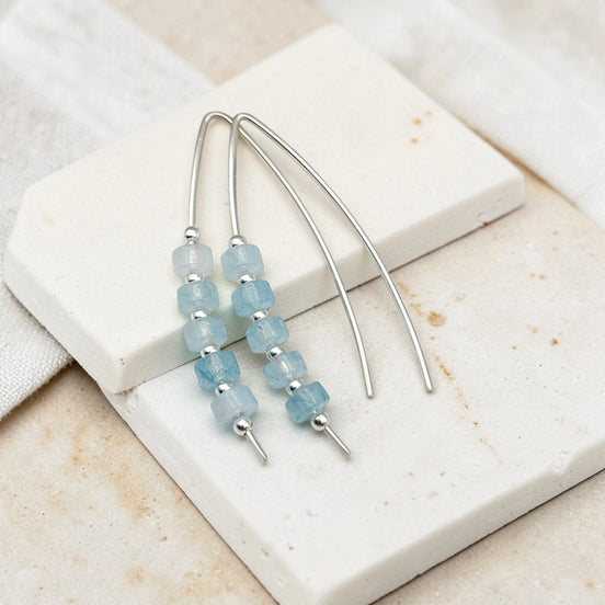 Silver earrings with aquamarine blue beads on a white stone surface