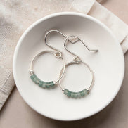 Silver hoop earrings with green aventurine beads on a white dish