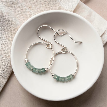 Silver hoop earrings with green aventurine beads on a white dish