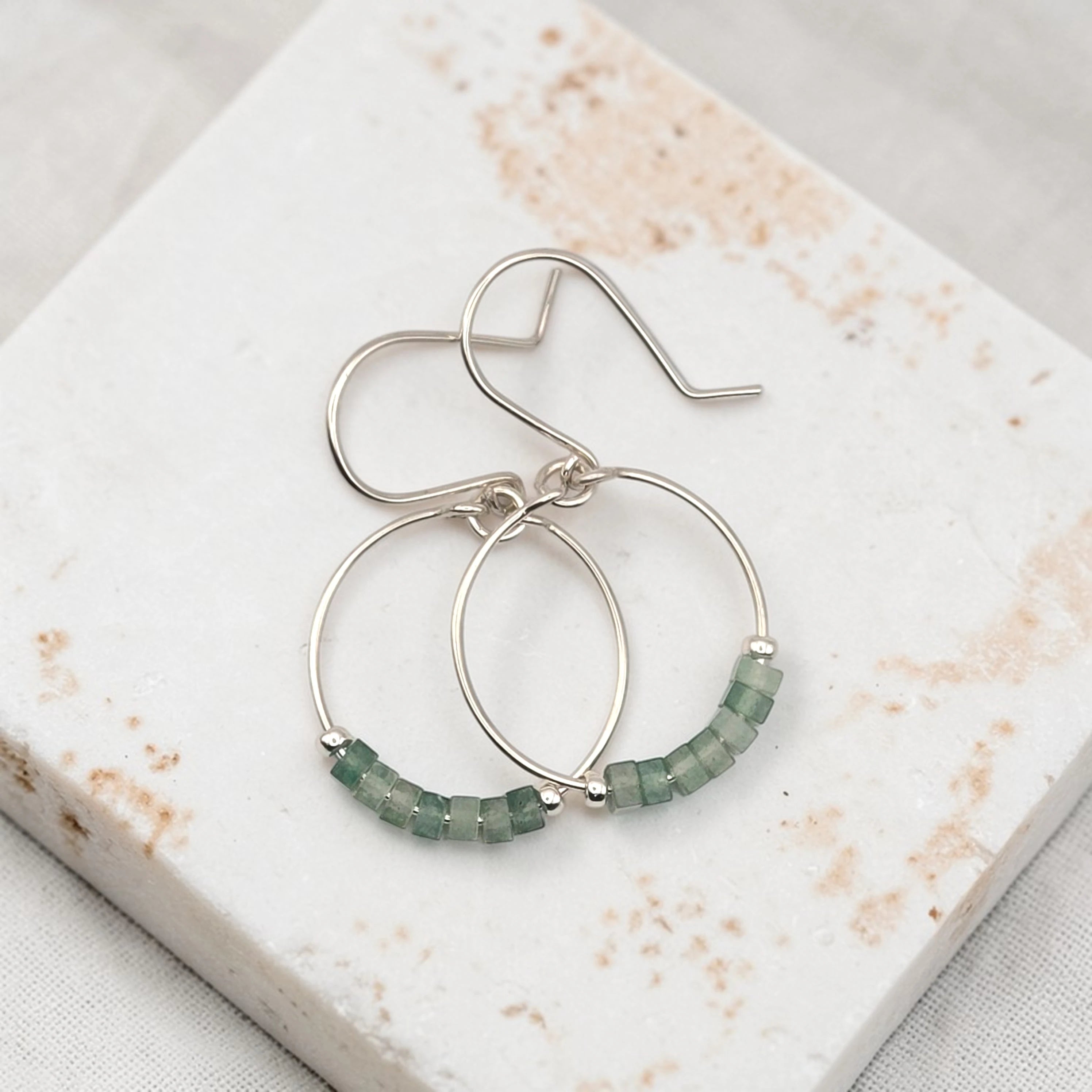 Silver hoop earrings with green aventurine beads on a marble surface